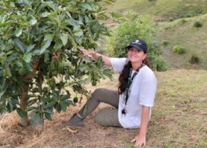Una giovane donna, vestita con un cappellino da baseball e un cappello, cammina in una montagna ricca di vegetazione Nella sua mano destra stringe un avocado, mentre nella sinistra una scarpa È unadolescente che si gode la tranquillità della natura!